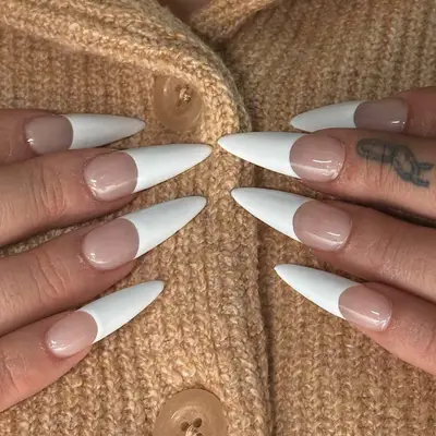 A close-up view of French manicured nails with pointed tips on hands placed on a knitted sweater