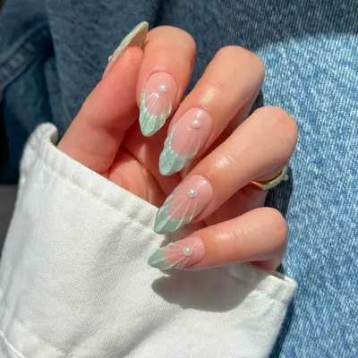 A hand displaying manicured fingernails with light blue French tips and pearl accents, with a denim jacket sleeve visible in the background