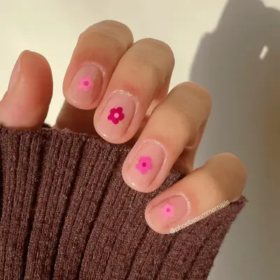 Short nude nails with dainty simple floral designs seen in multiple pink shades.