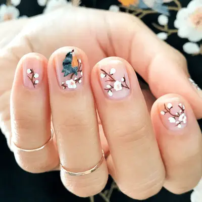 A close up of short nails with white cherry blossom branches and a blue bird.