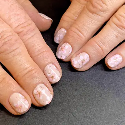 Close up of short nude nails with hand painted white cherry blossoms. 