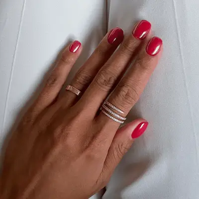 Close up of a red chrome manicure against a pair of blue jeans
