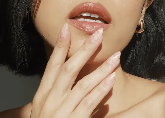 woman holding up fake nail manicure to chin 