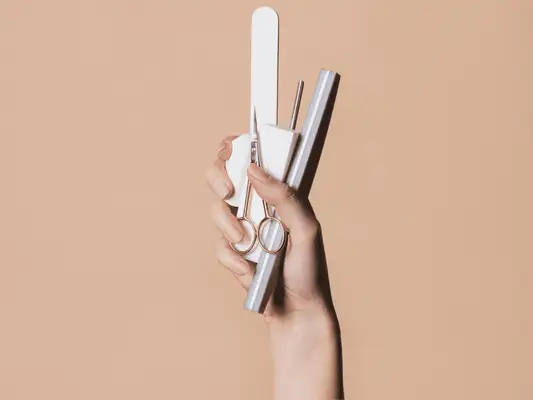 A hand holding nail tools including files, a buffer, scissor, cuticle pusher, and more