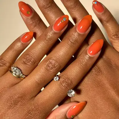 orange almond-shaped nails with metallic sticker accents