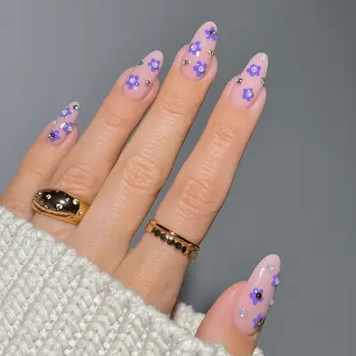 A manicure with a neutral base and sparkly purple floral details