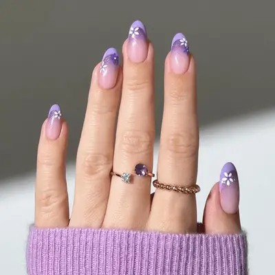 Close up of a French manicure with glitter faded underneath the tip and floral nail art.