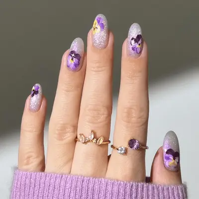 Close up of silver glitter nails with purple and yellow pressed floral pansies. 