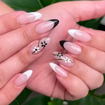 Black and white almond-shaped French manicure with matching floral and gold swirl motifs on the ring finger