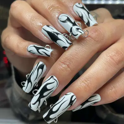 Long white square-shaped nails with abstract black swirls and silver piercings at the edges