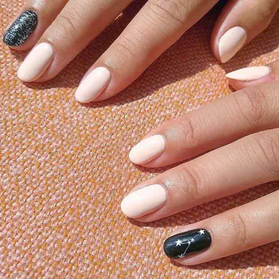 White nails with black celestial-inspired designs on the ring fingers