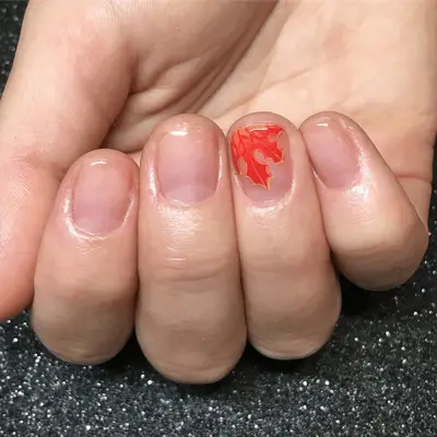 Close up of short glossy nails with an orange maple leaf on the ring finger.
