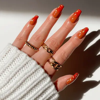 Close up of an orange ombre manicure, with gold leaf accents.