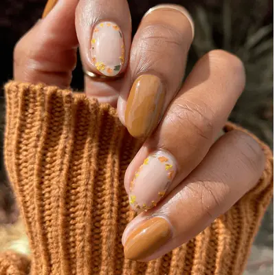 Close up of brown nails with yellow, green, and orange dried flowers on the perimeter of nude accent nails.