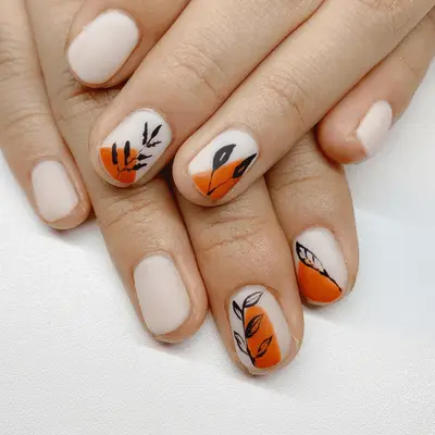 Close up of milky white short nails with orange triangle and black leaf detailing.