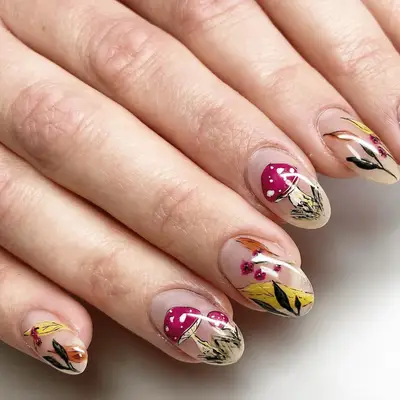 Close up of detailed cottagecore-inspired nail art, including toadstools and fall leaves.