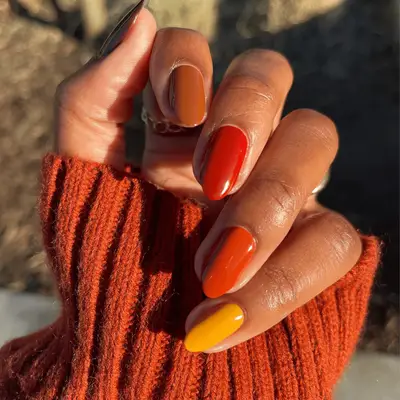 Close up of oval nails with alternating shades of orange, brown, red and yellow on each nail.