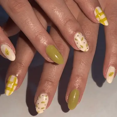 Close up of green and cream nails with green leaf and gingham nail art.