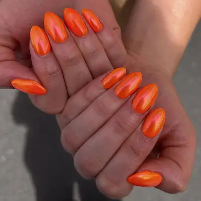 Hands with orange chrome manicure, close-up of nails
