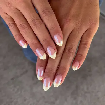Hands with manicured nails styled in a yellow and chrome French tip design