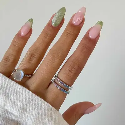 Hand with light green sparkly nail polish with white snowflake accent nail.