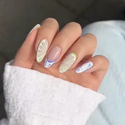A hand with nail art featuring lime slice designs and accents on each nail