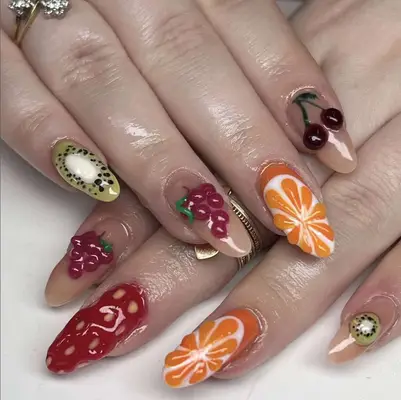 Close-up of hands with fruit-themed nail art featuring designs of cherries, oranges, grapes, kiwi, and strawberries