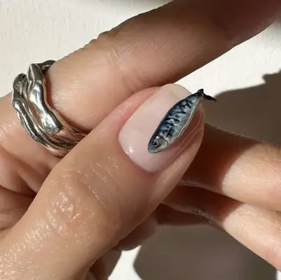 A hand with detailed nail art featuring a fish design, showing intricate craftsmanship