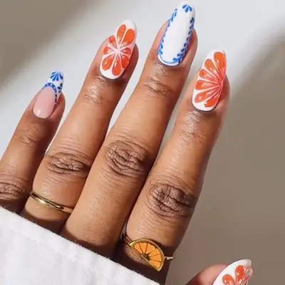 Hand displaying nail art with floral and patterned designs, wearing gold rings with one featuring an orange design