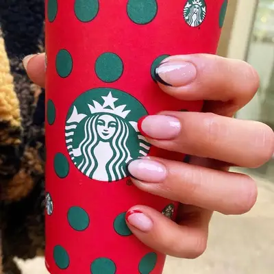 Hand with alternating green and red-tipped French manicure holding holiday Starbucks cup