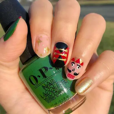 Christmas nails with red, green, gold, and black Nutcracker design holding polish bottle