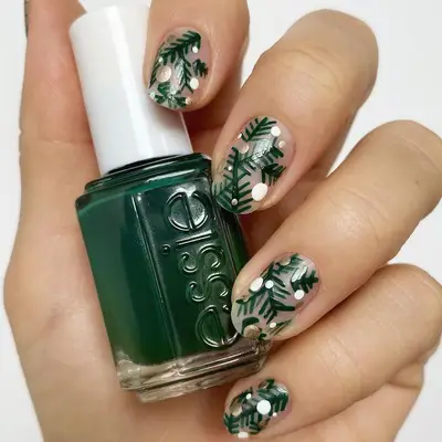 Hand with green, white, and silver evergreen nail design holding green Essie polish bottle