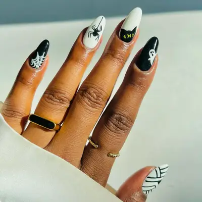 Black and white manicure with different Halloween motifs on each nail, including a spider web, spider, black cat, ghost, and mummy.