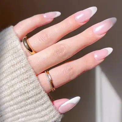 Hand with manicured nails featuring a classic white chrome French tip design, jewelry worn on ring fingers