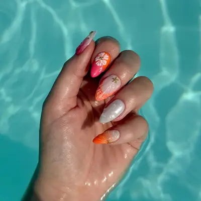 A hand with a manicure featuring mix-and-match designs under water, with patterns of coral, white, and orange