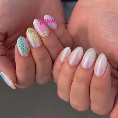 A pair of hands showing nails with colorful dotted designs on a white base, held in a closeup view