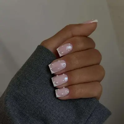 Manicured hand with French square nails, pearl and chrome detailing on an individual wearing a gray sleeve