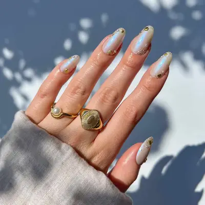 Hand with detailed nail art and gold rings, featuring seashell-inspired design