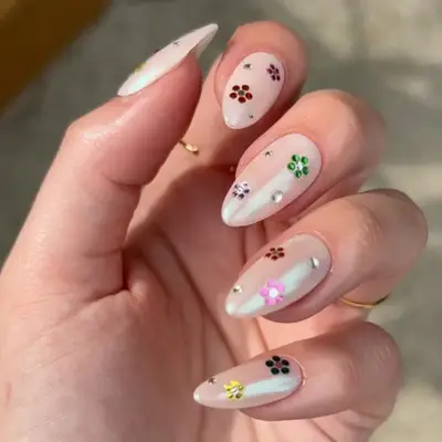 Hand with nail art featuring small floral designs and gem accents