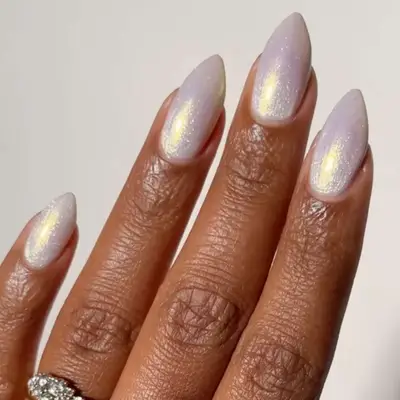 Close-up of a hand with pointed nails featuring a frosted white chrome finish, wearing a ring with a decorative design