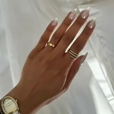 A hand with manicured nails in a minimalist style, wearing multiple rings and a wristwatch