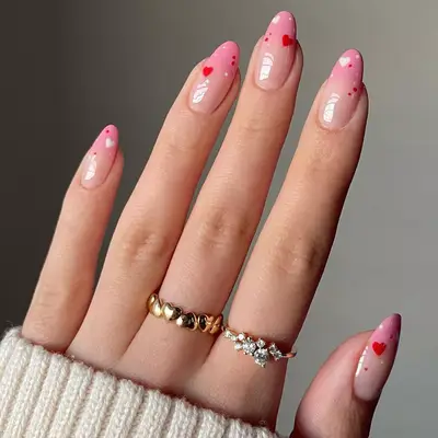 Hand with pink ombre base with mini red and white hearts painted at the tip.