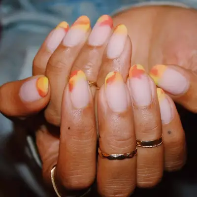 Hand with yellow, orange, and red tie-dye ombre French tip manicure