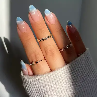 Hand with a light blue ombre manicure with hand-painted cloud designs
