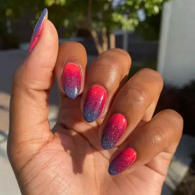 Hand with hot pink to navy blue gradient manicure with glitter finish