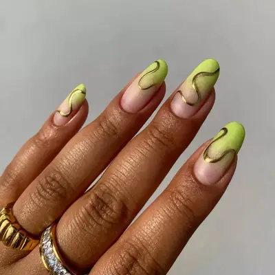 Hand with lime green gradient manicure with gold swirl detailing.