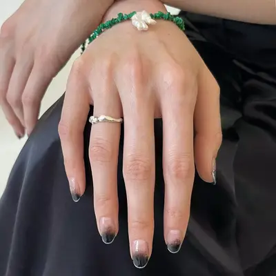 Hand with black ombre manicure with a thin silver French tip