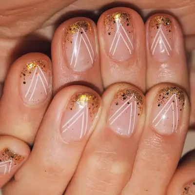 Hand with a gold glitter ombre manicure with a thin white chevron pattern