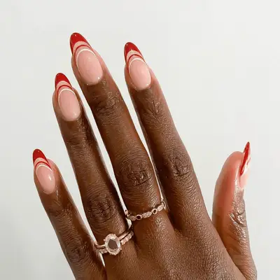 Almond-shaped nails with neutral pink base and red and white openwork French tips