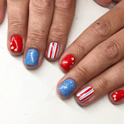 Close up of short nails with glitter blue accent nails, pinstripe prints, and stars
